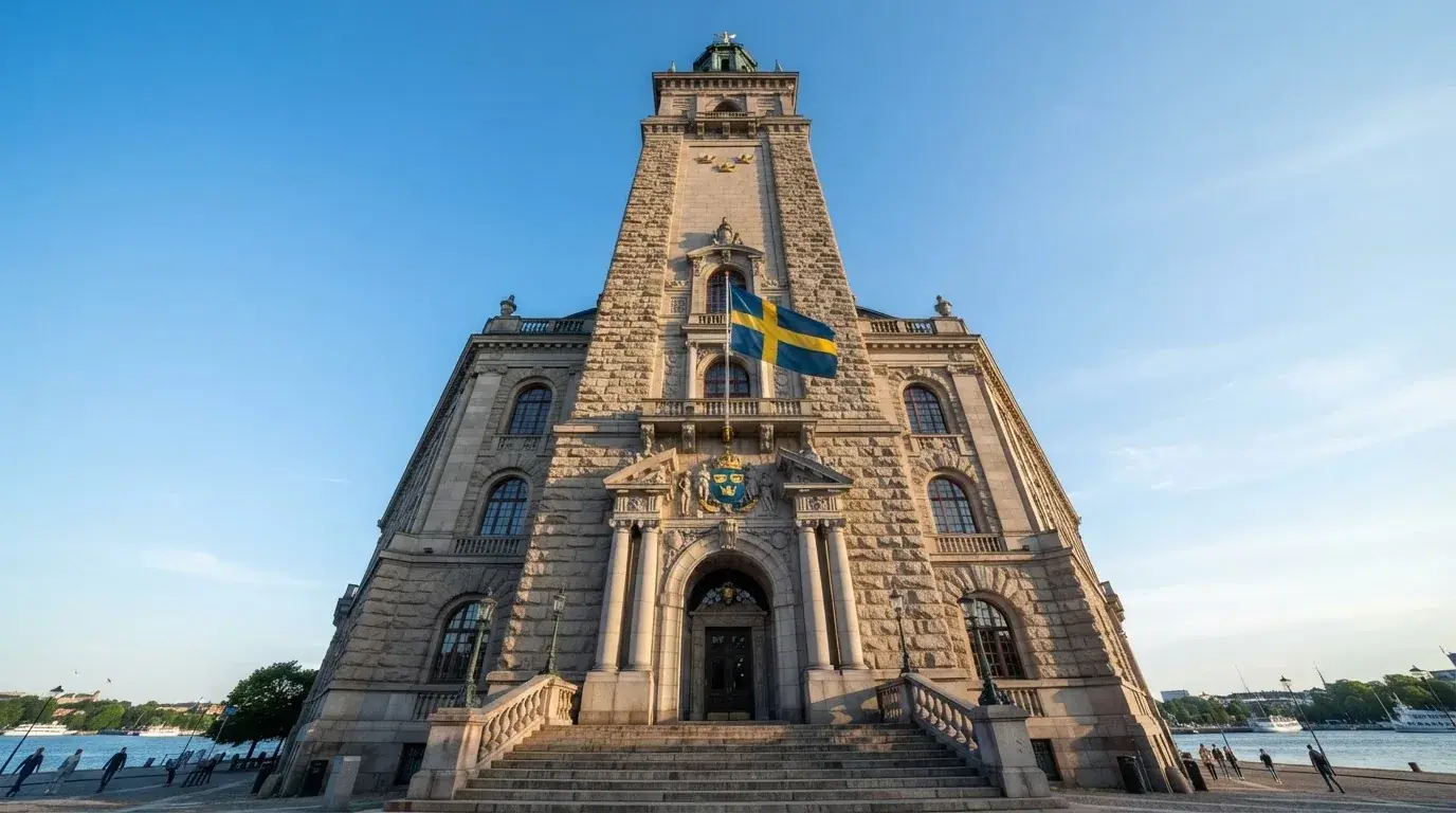 Ett gammalt stadshus i sten fotograferat underifrån mot en klarblå himmel, med den svenska flaggan som fladdrar ovanför entrén.